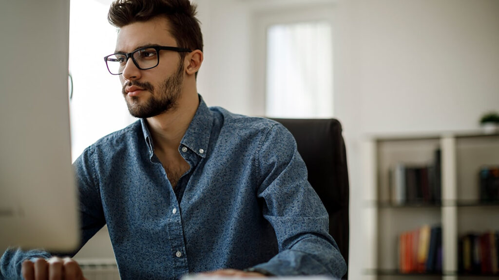 Man in blue shirt working at desk looking at monitor