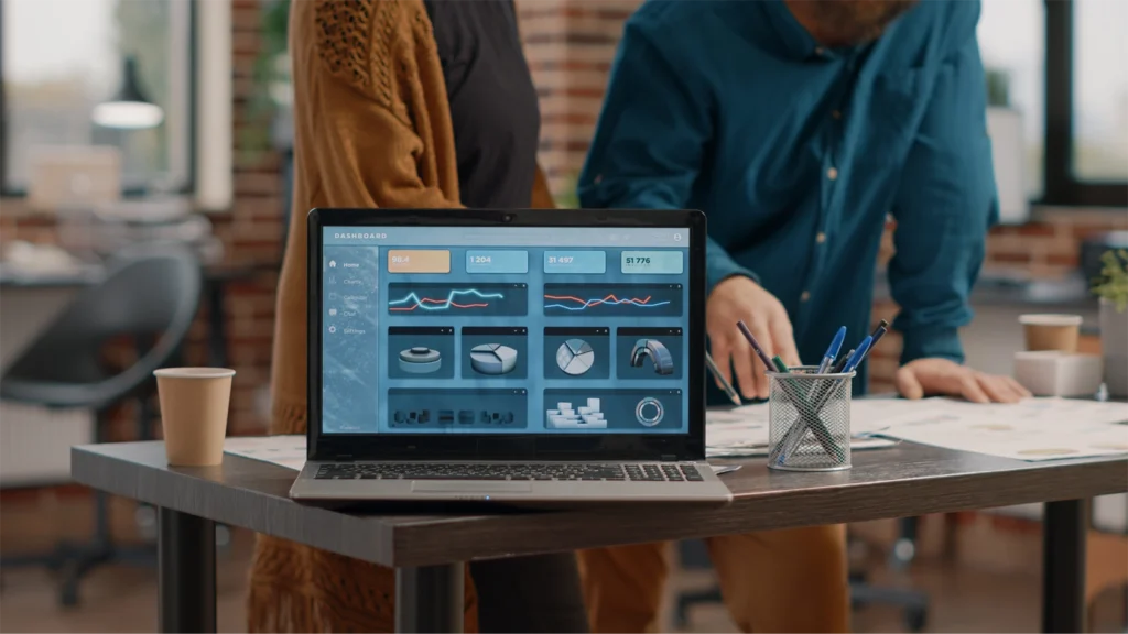 an image of a laptop on a desk with a dashboard of analytics graphs and event data on the screen. Behind the desk stand two colleagues looking at further data.
