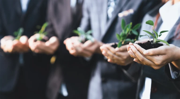 A line of people in suits with their hands extended cupping a small pile of earth and a green plant sprout