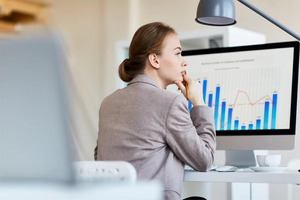 A woman sitting at a desk with a large monitor. There is a bar graph on the screen.