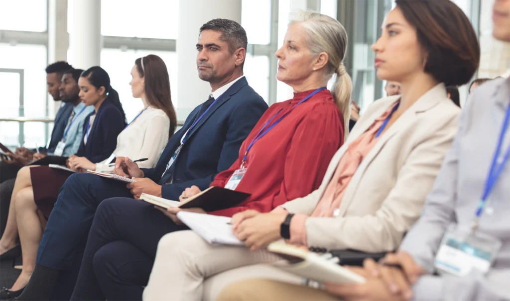 A group of business professionals sitting in a conference room in rows