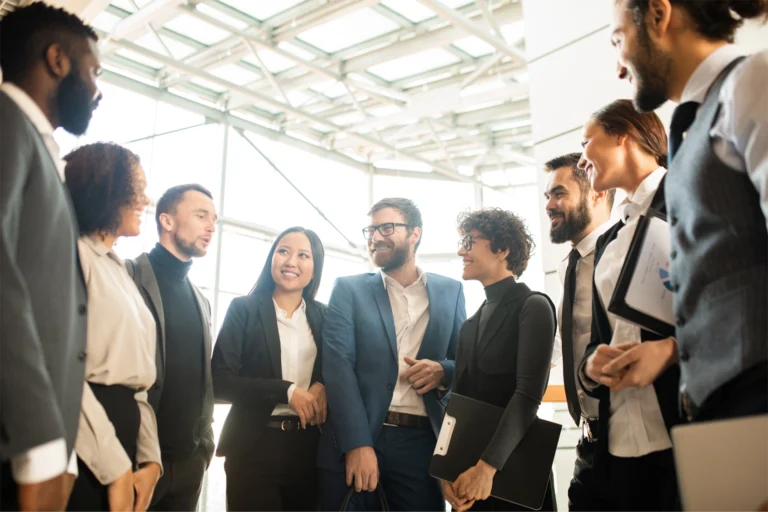 A group of business people standing in a semicircle engaging in a hybrid networking conversation