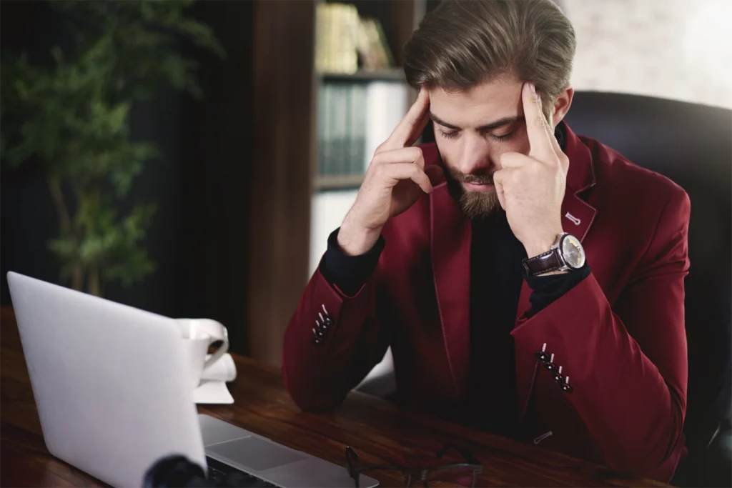 A man in a red suit holding his fingers to his temples as though stressed