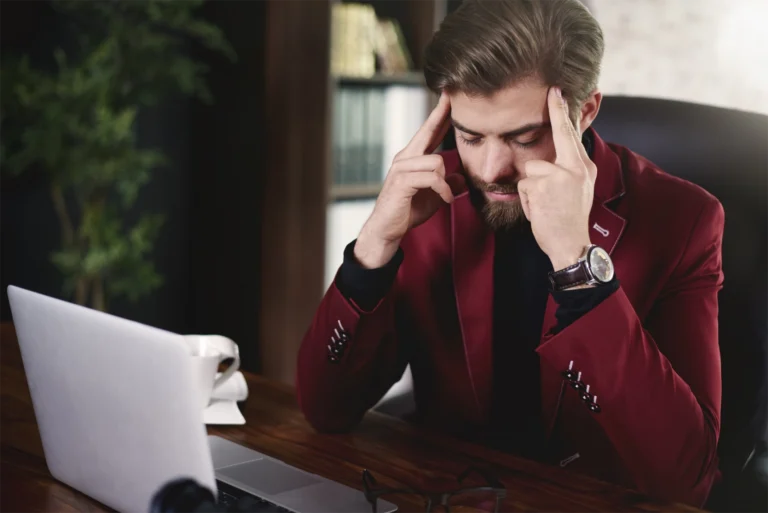 A man in a red suit holding his fingers to his temples as though stressed