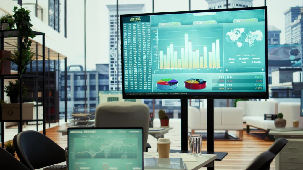 A boardroom with a table and chairs set up facing a screen with analytics dashboard display