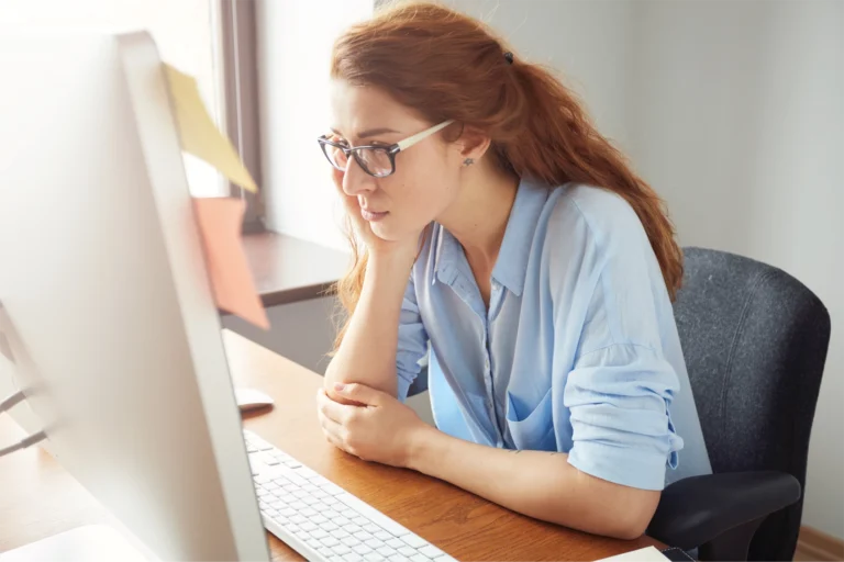 A woman sitting at a desk looking frustrated at her computer
