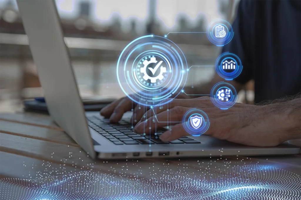 A close up of someone working at a laptop on a desk with glowing blue business continuity themed symbols floating above the keyboard